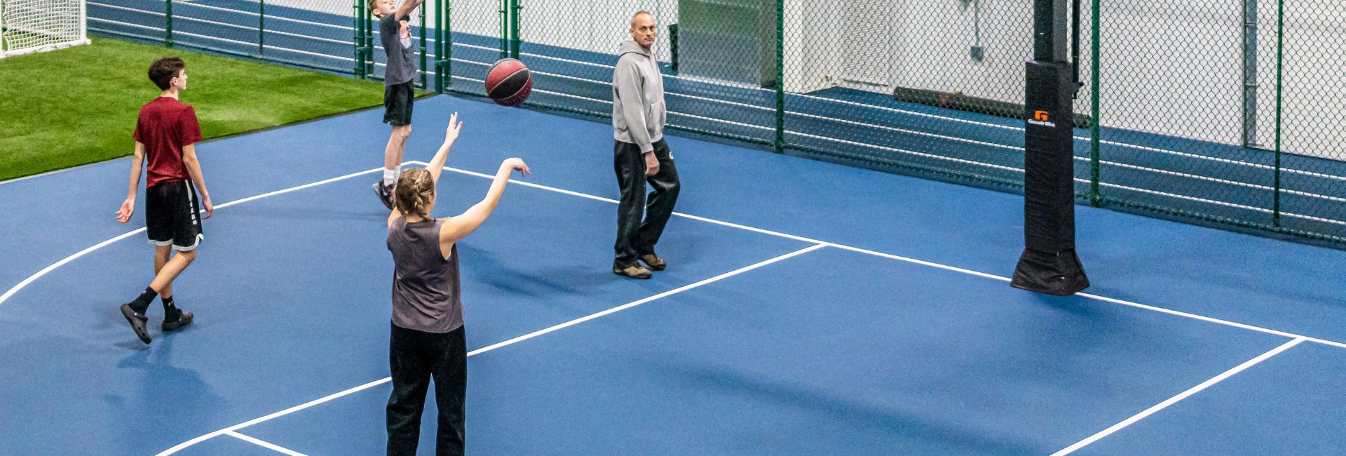 A group of people using the indoor basketball court at Janesville Athletic Club with multiple basketballs in play.